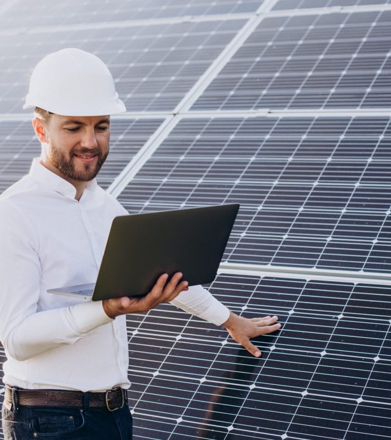 Young architect standing by solar panels making diagnostics on computer